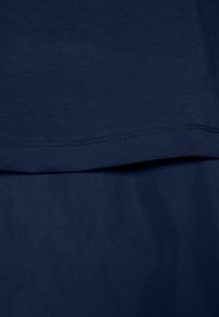 Marineblauem Stoff mit glatter Textur. Verfügt über ein geschichtetes Design mit sichtbaren Nähten an den Kanten. Schlichtes, minimalistisches Erscheinungsbild.