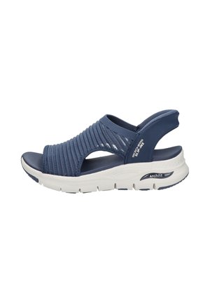 Navy blue slip-on sandal with stretchy knitted upper, cushioned white sole labeled "Arch Fit," and open heel strap for comfort and support.
