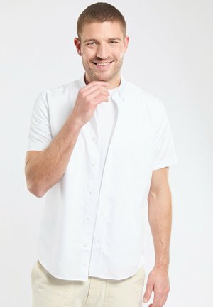 Chemise blanche à manches courtes en tissu léger, avec un devant à boutons, un col montant et une texture lisse.