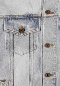 Jasnoniebieska kurtka dżinsowa z wyblakłym odcieniem, z metalowymi zatrzaskami, kieszenią na piersi i widocznymi detalami szycia. Teksturowany materiał.