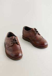 Brązowe skórzane buty eleganckie z perforowanymi detalami, sznurowane, z okrągłym noskiem. Charakteryzują się gładką teksturą i niskoprofilową gumową podeszwą.