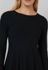 Robe noire à côtes, à manches longues, décolleté rond et ourlet évasé. La texture est lisse avec des détails en côtes verticales.