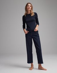 Navy long-sleeve top paired with dark denim, wide-leg jeans featuring raw hems. Bare feet, neutral background.
