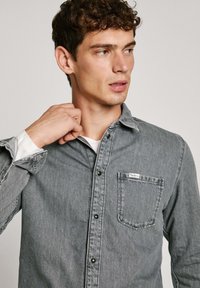 Grijze denimhemd met een knoopkraag, lange mouwen en één borstzak. Bevat een logo-label. Zachte textuur en klassieke pasvorm.