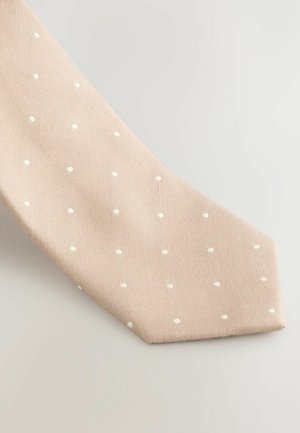 Cravat bej cu o suprafață texturată, cu buline albe uniform dispuse, îngustându-se către un vârf ascuțit. Design clasic dintr-un material neted.