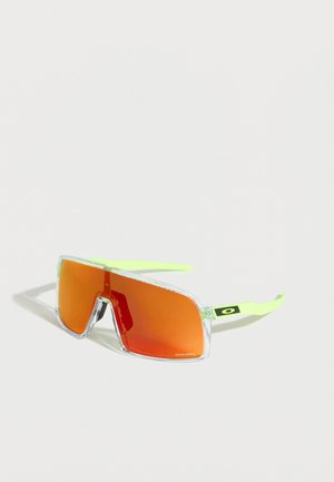 Oversized zonnebril met doorzichtige monturen, neongele pootjes en grote oranje getinte glazen met Oakley-logo aan de zijkant.