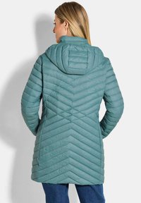 Gevoerde jas in gedempt teal, met chevronstiksel, een capuchon en een middelange snit. Glad textuur met een slank ontwerp.