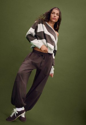 Un sweat à rayures oversized en gris et marron, associé à un pantalon large marron foncé. Il présente une coupe décontractée et une taille élastique, avec des chaussures sportives.