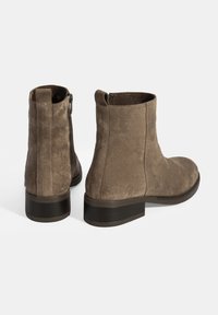 Bottes chelsea en suède brun avec une texture lisse, bout arrondi et un petit talon bloc. Elles disposent d'une fermeture éclair sur le côté pour un enfilage facile.
