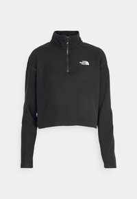Pull polaire court noir avec fermeture éclair quart de tour et logo blanc "The North Face" sur la poitrine, manches longues et col montant.