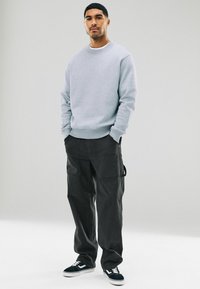 Sudadera de algodón gris con puños y cuello acanalados, combinada con pantalones cargo oscuros que tienen múltiples bolsillos y zapatillas negras.