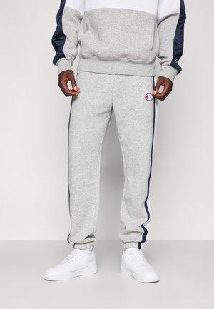 Pantalones de chándal grises con rayas laterales en azul marino y un logo bordado. Hechos de tela suave, cuentan con puños acanalados y cintura con cordón.