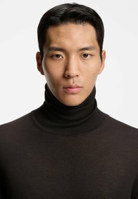 Ciemnobrązowy sweter z golfem wykonany z gładkiego, drobno dzianego materiału. Posiada wysoki kołnierz i dopasowany krój. Minimalistyczny design.