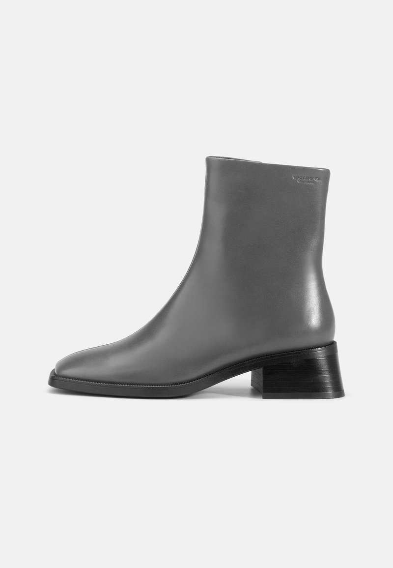 Bottine grise en cuir avec bout carré, talon bloc, et logo de marque embossé près du bord supérieur sur une surface lisse.