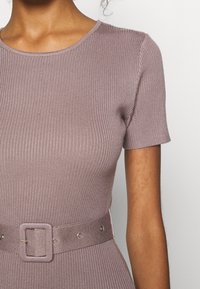 Gros plan d'une personne portant une robe mauve côtelée à manches courtes avec une ceinture en tissu assortie munie d'une boucle carrée.