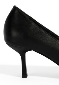 Zwarte hoge hak met een gladde, textuur oppervlak, spitse neus en een slanke, vierkante hak voor stabiele ondersteuning.