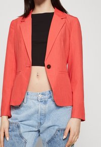 Korallfärgad tygblazer med notch-laplar, enknappsstängning och två framfickor. Matchas med högmidjade ljusblå jeans.