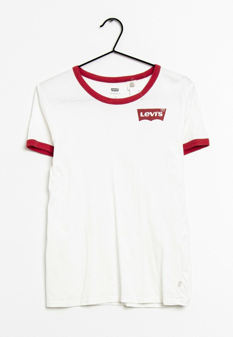 Camiseta blanca de Levi's con cuello y borde de las mangas en rojo, colgada en una percha negra sobre fondo blanco.