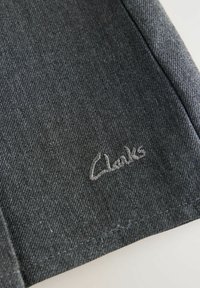 Tessuto grigio con una superficie liscia e testurizzata, presenta un logo ricamato "Clarks" in un grigio più chiaro. Cuciture visibili lungo i bordi.