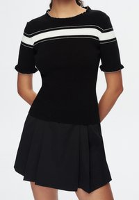 Top de punto negro con mangas cortas con volantes, que presenta rayas horizontales blancas en el pecho. Combinado con una falda negra con plisados.