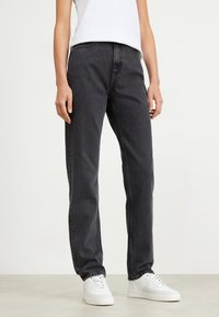 Jeans de denim negro con un corte recto, que presentan un diseño clásico de cinco bolsillos y detalles de costura sutiles, combinados con zapatillas blancas.