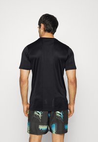 Camiseta atlética negra de manga corta, con un panel trasero texturizado. Combinada con pantalones cortos con un patrón en tonos oscuros y acentos en azul claro.