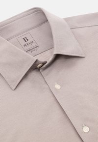 Camisa de hombre en marrón claro con finas rayas verticales blancas, que cuenta con un collar clásico y dos botones en el tapeta. Textura suave.