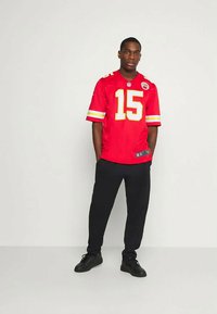 Raudona futbolo marškinė su geltonais akcentais ir numeriu 15, derinami su juodomis kelnėmis ir sportbačiais. Marškiniai turi NFL logotipą krūtinėje ir rankovėse.