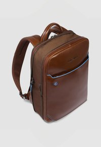 Mochila de cuero marrón con un diseño estructurado, detalles en azul contrastante, un bolsillo delantero y correas de hombro acolchadas y ajustables.