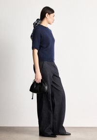 Μπλε ναυτικό πουλόβερ με κοντά μανίκια από μίγμα μοχέρ, φαρδιά παντελόνια μαύρου τζιν, μαύρη δερμάτινη τσάντα με κορδόνια και μυτερά μαύρα παπούτσια.