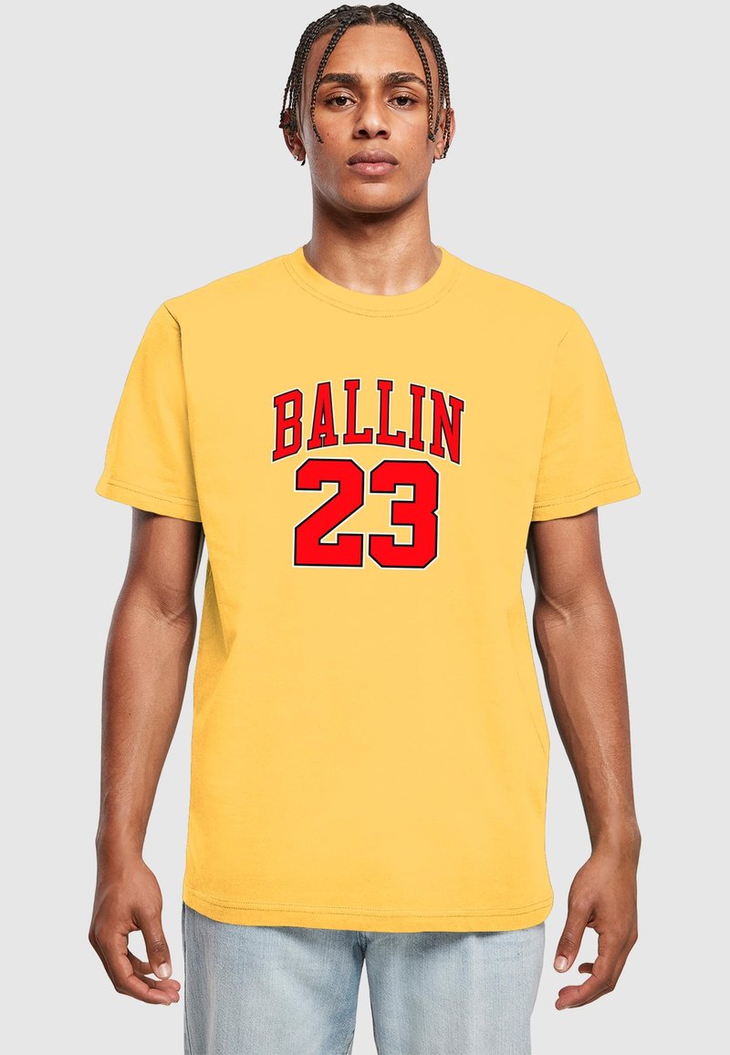 Žuta pamučna majica s velikim crvenim tekstom koji glasi "BALLIN" i brojem "23." Klasični okrugli izrez i kratki rukavi.