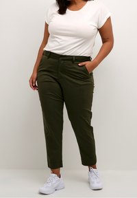 Pantalon vert olive coupe droite, passants de ceinture, poches avant et ourlets retroussés, associé à un T-shirt blanc ajusté et des baskets blanches.