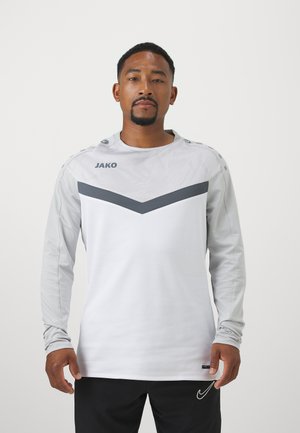 Langarm sportshirt in het wit met een grijs chevronontwerp. Gemaakt van ademend materiaal, met een logo op de borst en schouderknopen.