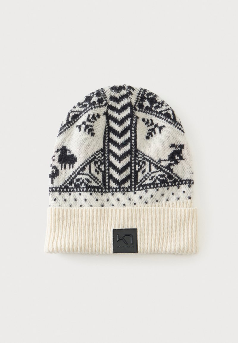 Bonnet blanc tricoté avec des motifs nordiques noirs comprenant des animaux, des formes géométriques, et un revers côtelé plié avec un patch logo noir.