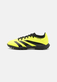 Botas de fútbol amarillas y negras con un diseño elegante, parte superior texturizada y suela de goma con picos para tracción. Marca "Predator" visible.