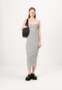 Vestido midi listrado em preto e branco, com um design sem alças, feito de material elástico. Usado com sapatos de plataforma pretos e robustos.