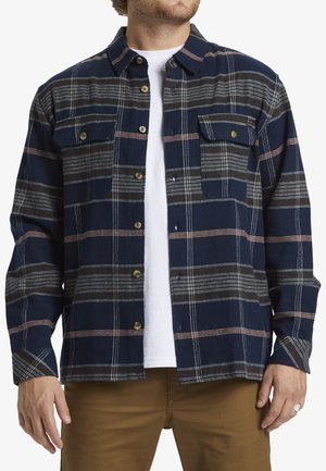 Chemise en flanelle navy avec un motif à carreaux, des rayures blanches et oranges, deux poches poitrine et fermeture à boutons. Matière en coton, coupe décontractée.