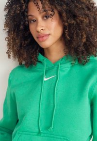 Green cotton hoodie with a front pocket, drawstring hood, and white Nike logo. Features a soft texture and relaxed fit.