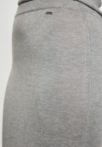 Šedá bavlněná sukně s hladkou texturou, přiléhavým střihem a malou kovovou logo značkou na elastickém pasu, s jednoduchým a minimalistickým designem.