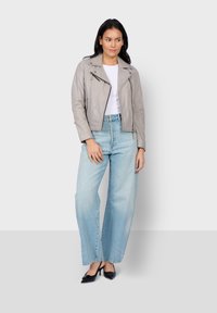 Giubbotto in pelle grigio cropped da motociclista con chiusure a zip, indossato sopra una maglietta bianca e abbinato a jeans a gamba larga blu chiaro e tacchi neri.