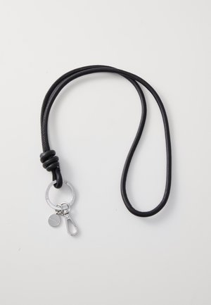 Cuerda negra con diseño anudado. Presenta un llavero plateado, un pequeño charm y un clip de metal para su sujeción. Textura suave.