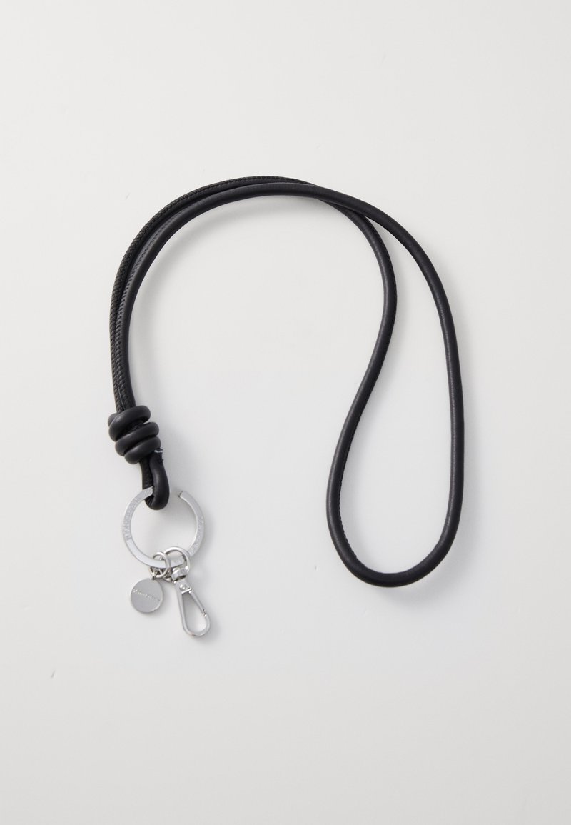 Cuerda negra con diseño anudado. Presenta un llavero plateado, un pequeño charm y un clip de metal para su sujeción. Textura suave.