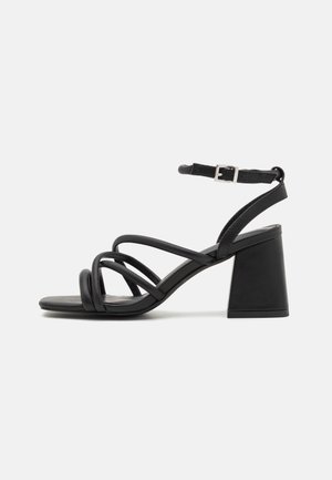 Sandalias de tacón de cuero negro con múltiples tiras delgadas, diseño de punta cuadrada y tacón ancho. Correa ajustable en el tobillo con detalle de hebilla.
