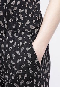 Tela negra con un patrón de cachemira blanca, presenta un bolsillo frontal y una cintura elástica. Textura suave con un diseño de corte relajado.