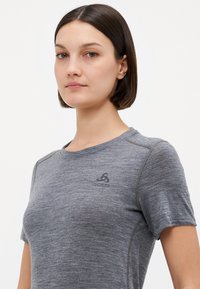 T-shirt de sport gris à manches courtes, encolure ronde et petit logo sur la poitrine gauche. Texture douce avec un motif chiné subtil.