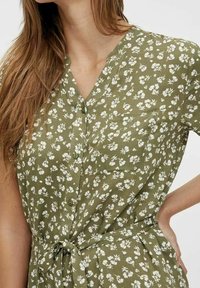 Olivgrünes Kleid mit weißem Blumenmuster, durchgehender Knopfleiste, kurzen Ärmeln und Bindegürtel in der Taille. Leichter Stoff mit weicher Textur.