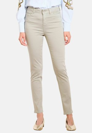 Beige slim-fit kalhoty, nošené s nízkými zlatými podpatky a zasunutou dlouhou košilí s vyšívanými rukávy.