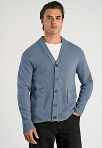 Ljusblå cardigan i stickad tyg med sjalkrage, fem svarta knappar och två framfickor. Ribbstickade ärmslut och nederkant.