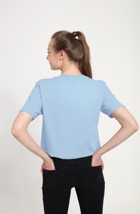 Lyseblå kortærmet t-shirt med rund hals, lavet af bomuldsstof. Modellen har sorte jeans på, hænderne i lommerne.