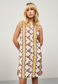 Robe sans manches avec des motifs géométriques multicolores en orange, jaune, bleu et rouge sur un fond blanc, présentant une coupe décontractée.